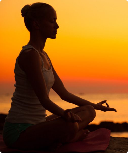 A woman sitting in the sunset doing yoga.