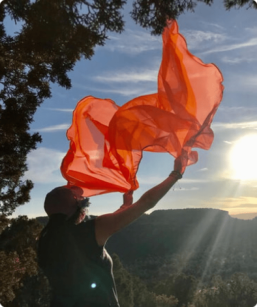 A person holding up orange flags in the sun.
