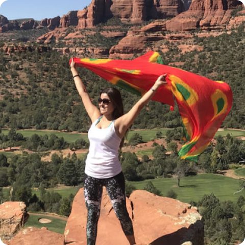 A woman standing on top of a mountain holding up a red and yellow flag.