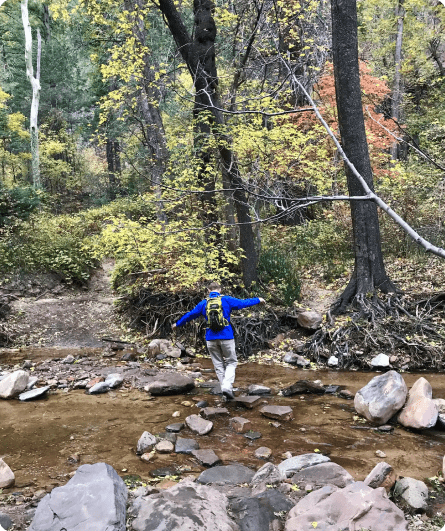 A person in blue jacket standing on rocks near water.