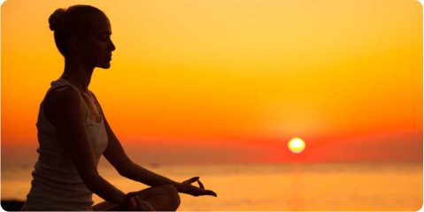 A person sitting in the sunset doing yoga.