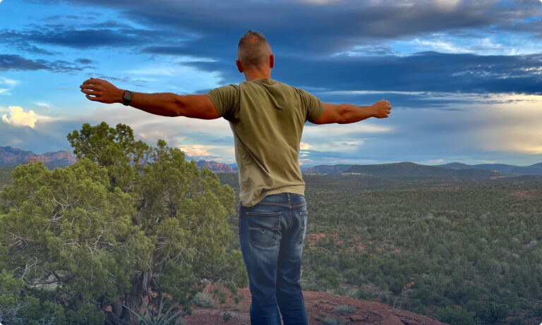 A man standing on top of a hill with his arms outstretched.